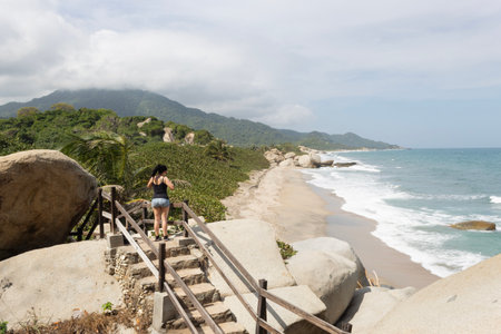 Young woman at the top of a trekking path stairs into Colombian Tayroina national park with Sierra Nevada mountain range and Caribbean sea at background in sunny dayの写真素材