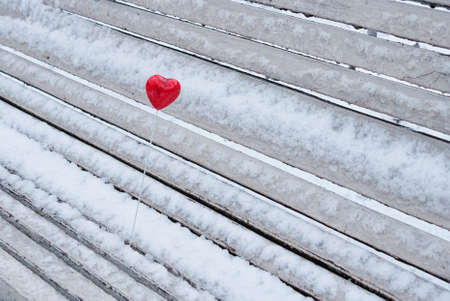 Red lollipop heart shaped on the snowy bench in winter parkの写真素材