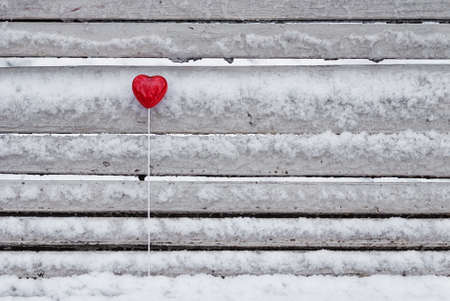 Red lollipop heart shaped on the snowy bench in winter parkの写真素材