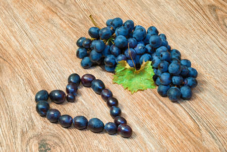 Blue bunch of grapes and heart shaped grapes on a wooden textureの写真素材
