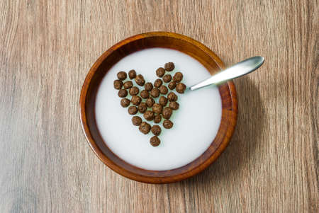 Heart shaped cereal chocolate balls in wooden bowl with milkの写真素材