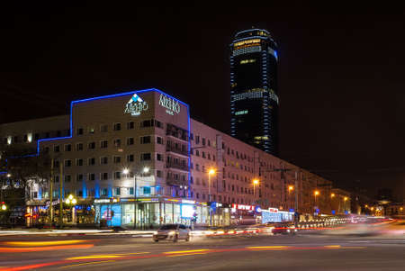 Yekaterinburg, Russia - December 27, 2015: Night crossroad with blurred traffic. The photo shows the hotel building called the "Avenue" with shops on the ground floor. Against the background - a skyscraper of business center "Vysotsky"のeditorial素材