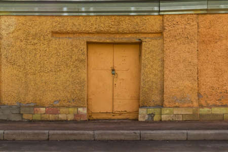 Locked iron door in yellow concrete wall front viewの写真素材