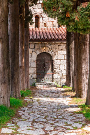 Stone walkway with trees and a door in the wall of the stone churchの写真素材