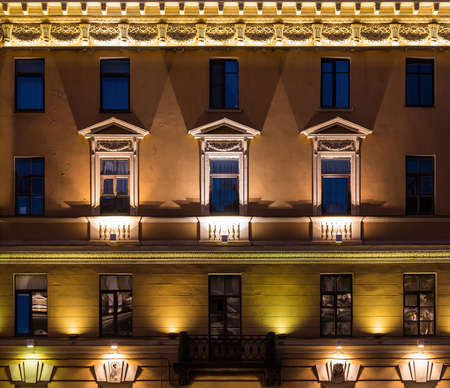 Several windows in a row and balcony on night illuminated facade of urban apartment building front view, St. Petersburg, Russiaの写真素材