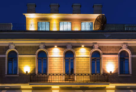 Several windows in a row and balcony on night illuminated facade and mansard of urban office building front view, St. Petersburg, Russiaの写真素材