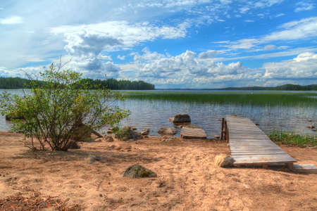Bush and pier on the sandy shore of the lake in summer sunny dayの写真素材