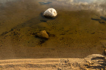 Stone in the clear water on the sandy shore of the lakeの写真素材