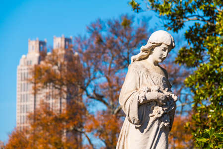 The sculpture of Virgin Mary closeup on the Oakland Cemetery on the background of skyscraper in sunny autumn day, Atlanta, USAの写真素材