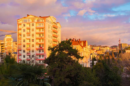 View of apartment buildings and trees on the background of beautiful cloudy sky at sunset, Sochi,...