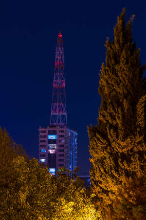 Apartment building and base station seen behind trees on the background of clear sky at dusk, Sochi, Russiaの写真素材