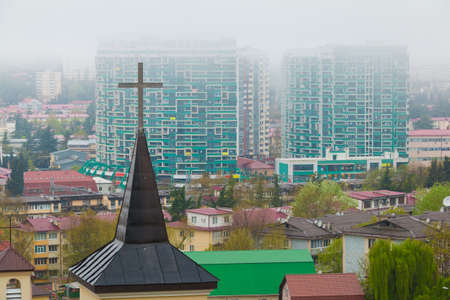 Aerial view of the cross of church on the background of apartment buildings in the morning fog, Sochi, Russiaの写真素材