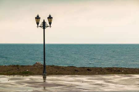 The lamppost standing on the embankment on the background of sea in rainy day