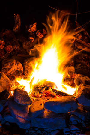 Campfire surrounded by rocks and a pile of firewood behind it at night