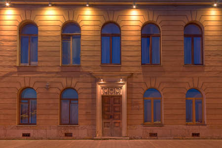 Several windows in a row and a door on a night illuminated facade of a urban apartment building. Petersburg, Russiaの写真素材