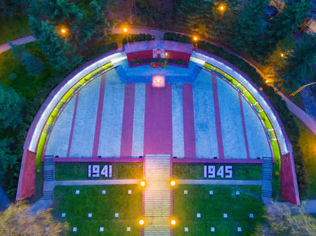 Top-down drone view of stairs, lawn and square with eternal flame of illuminated Zavokzalnyy Memorial Complex at twilight, Sochi, Russiaのeditorial素材