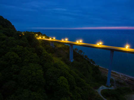 Drone view of the illuminated Zubova Schel viaduct and mountainside with forest on the background of the sea at dusk, Sochi, Russiaの写真素材