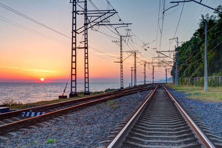 Beautiful landscape of a railroad and towers of traction line on the background of the sea at sunset, Sochi, Russiaの写真素材