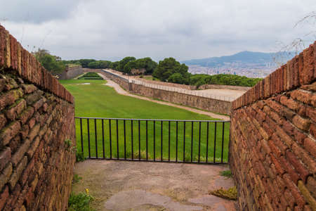 Aerial view of stone walls and lawn of the Montjuic Castle with two brick walls in the foreground in overcast day, Barcelona, Catalonia, Spainのeditorial素材