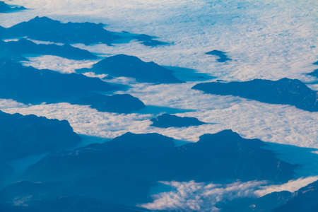 View from the porthole of airplane of a beautiful landscape with mountains hiding in the cloudsの写真素材