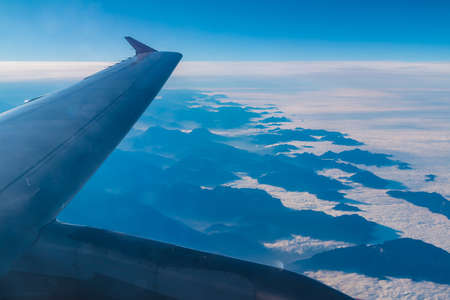 The wing of the airplane above a mountains hiding in the clouds closeup, view from the porthole