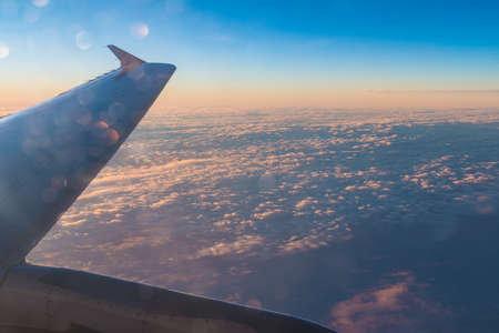 The wing of the airplane above the clouds closeup at sunset, view from the portholeの写真素材