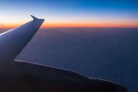 The wing of the airplane above the clouds closeup at sunset, view from the portholeの写真素材