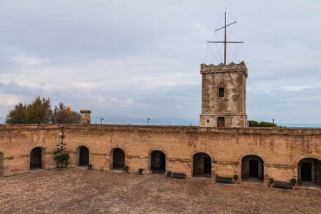 Barcelona, Catalonia, Spain - November 16, 2018: The tower and the courtyard of the Montjuic Castle with pavement, stone walls and arches in cloudy dayのeditorial素材