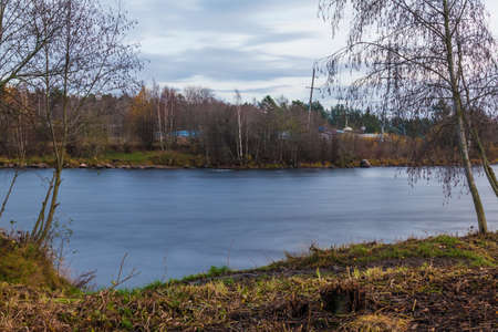 Long-exposure view of the Vuoksi River and bare trees in cloudy autumn day, Losevo, Leningrad Oblast, Russiaの写真素材