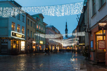 Tallinn, Estonia - December 25, 2018: Beautiful long-exposure view of buildings on the illuminated Viru Street in the Tallinn Old Town with a crowd of people blurred in motion in overcast winter day at twilightのeditorial素材