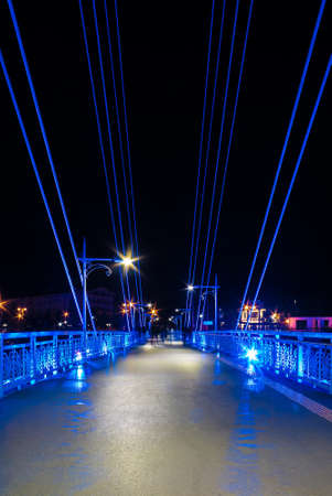 Perspective view of illuminated span of the Bridge of Lovers with people blurred in motion at night, Tyumen, Russiaの写真素材