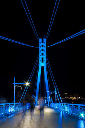 Perspective view of illuminated span and pylon of the Bridge of Lovers with people blurred in motion at night, Tyumen, Russiaのeditorial素材