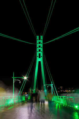 Perspective view of illuminated span and pylon of the Bridge of Lovers with people blurred in motion at night, Tyumen, Russiaのeditorial素材