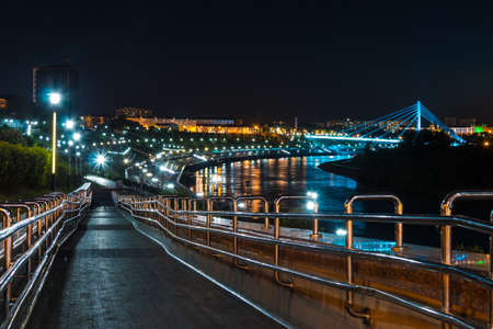Beautiful view of the illuminated Embankment of Tura River and the Bridge of Lovers at dusk, Tyumen, Russiaの写真素材