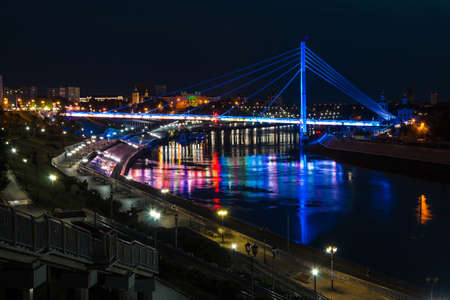 Beautiful view of the illuminated Embankment of Tura River and the Bridge of Lovers at dusk, Tyumen, Russiaの写真素材