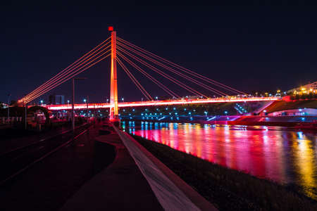 Beautiful view of the illuminated Bridge of Lovers over the Tura River at dusk, Tyumen, Russiaの写真素材