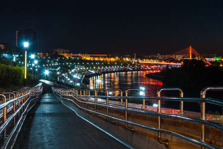 Beautiful view of the illuminated Embankment of Tura River and the Bridge of Lovers at dusk, Tyumen, Russiaの写真素材