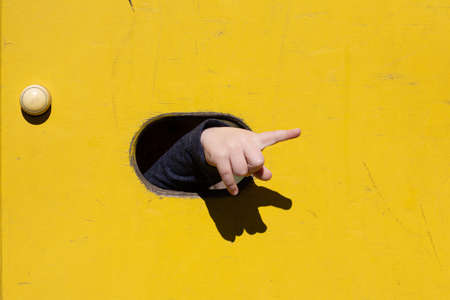 Child pointing finger to the right through a hole on a yellow backgroundの写真素材