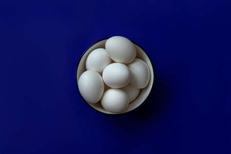 white eggs in a plate on a blue background postcard for easter minimalismの写真素材