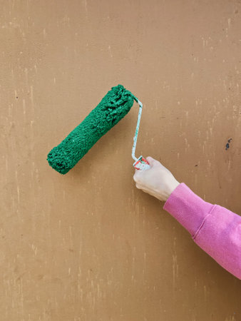 female hand with a roller for painting the wall in green. home renovation in springの写真素材