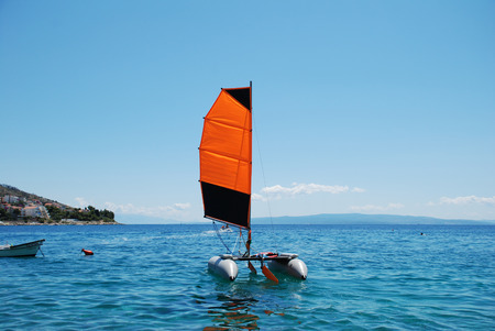 Inflatable catamaran with orange sail on the background of the sky and the seaの写真素材