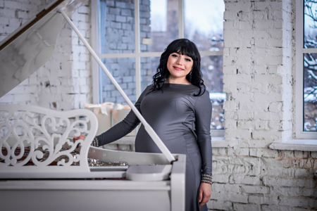 Pregnant woman in the gray dress stands near white piano and the window, winter landscape outsideの写真素材