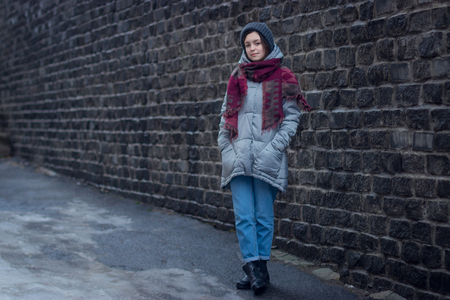 Sad girl stands near a wall in jacket hat and scarfの写真素材