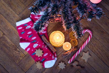 A candle is burning under the Christmas tree, near are cookies, candy, wool socks and mittens.の写真素材