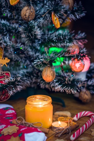 A candle is burning under the Christmas tree, near are cookies, candy, wool socks and mittens.の写真素材