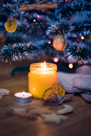 A candle is burning under the Christmas tree, near are cookies, candy, wool socks and mittens.の写真素材