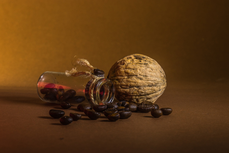 a small bottle with coffee beans and walnut on a brown background.の写真素材