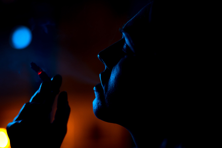 girl at the window smoking a cigarette in the night light, silhouette.の写真素材