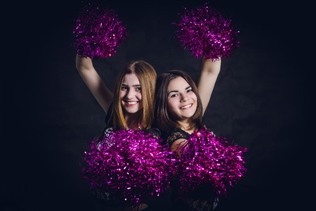 Two professional cheerleaders posing at studio on black screen.