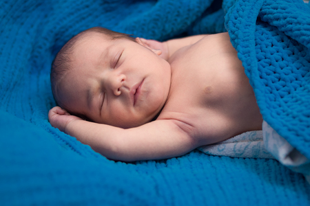 newborn baby sleeping on the bed under a blue blanket.の写真素材